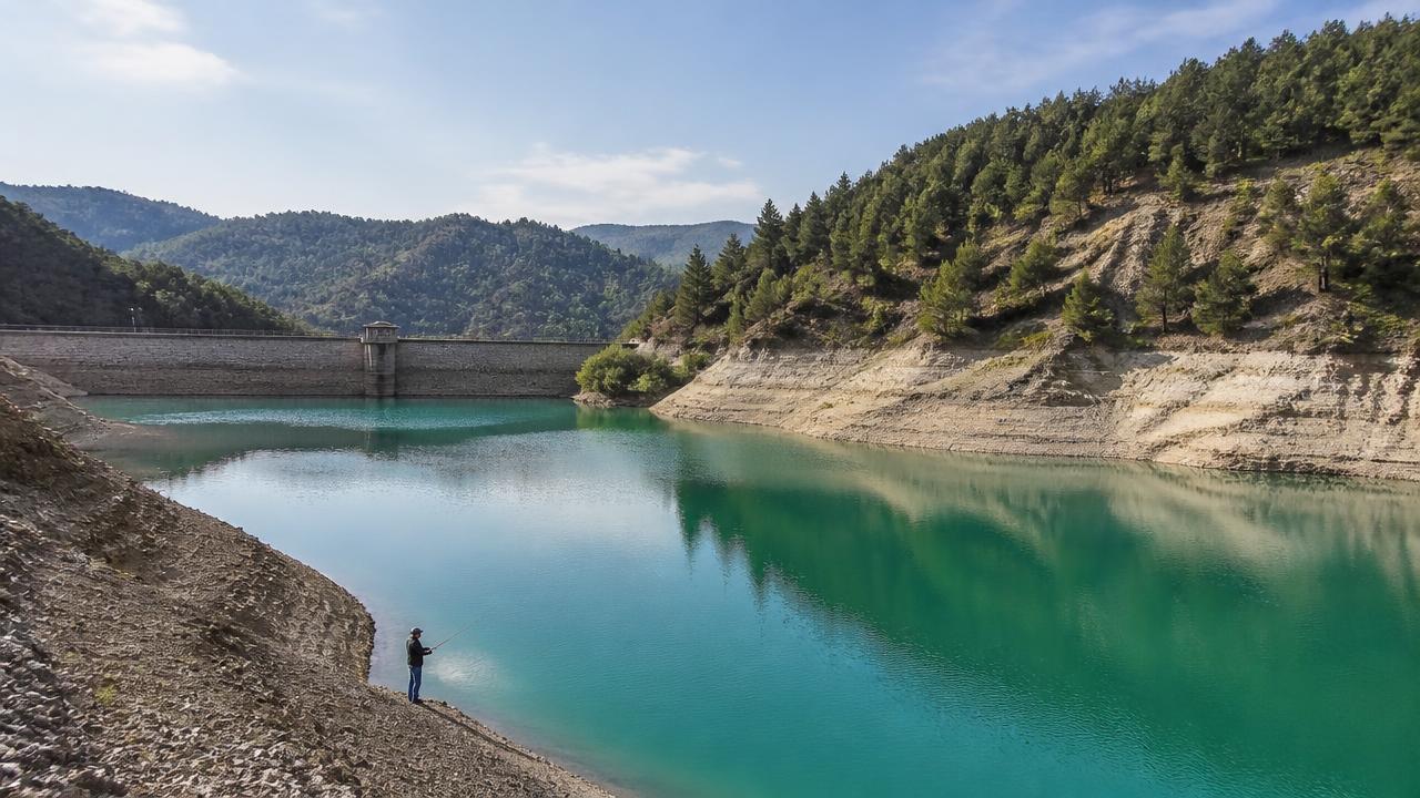 Wide view across a large Cyprus reservoir surrounded by hills, with an angler on the distant bank