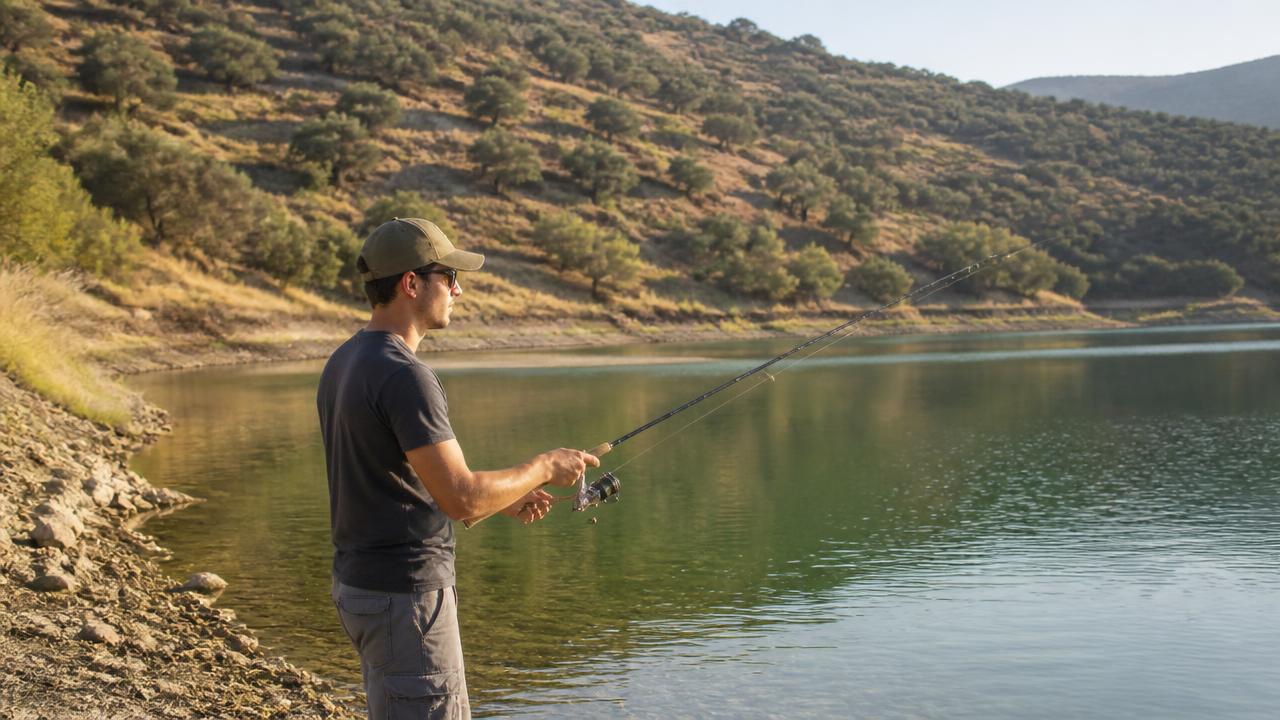 A beginner angler casting a spinning rod from the bank of a Cyprus reservoir at dawn
