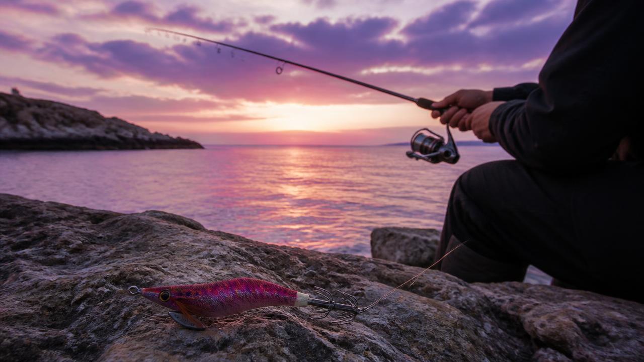 Eging setup with a Japanese-style squid jig beside a rocky Cyprus harbour at dusk